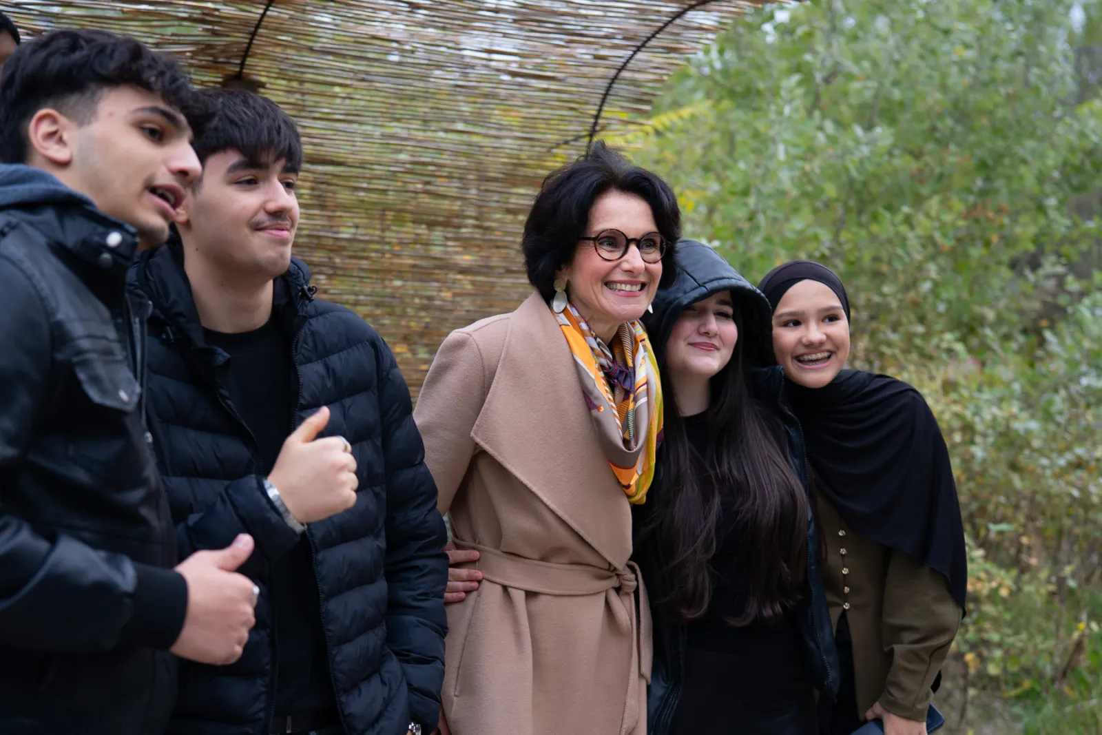 Gruppe von fünf Personen posiert fröhlich für ein Gruppenfoto im Freien, vor grünem Hintergrund, unter einem Schilfdach.