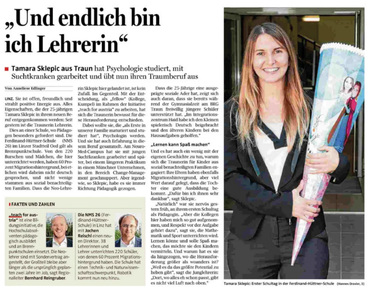 Person im Blazer lächelt und hält eine große Posterrolle; steht vor einer Gebäudetür.