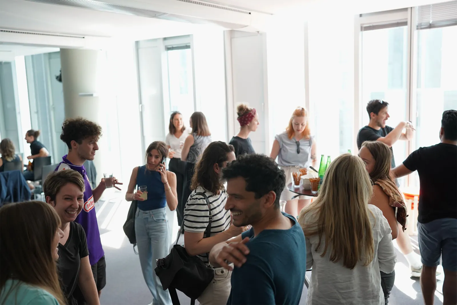 Gruppe junger Erwachsener unterhält sich bei informellem Empfang in hellem Büro, einige halten Getränke.