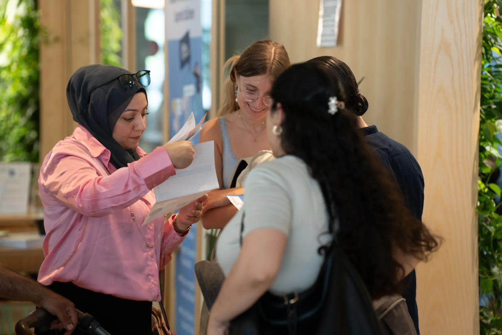 Person im Hijab übergibt Unterlagen an mehrere Personen an einem Informationsstand in Innenraum