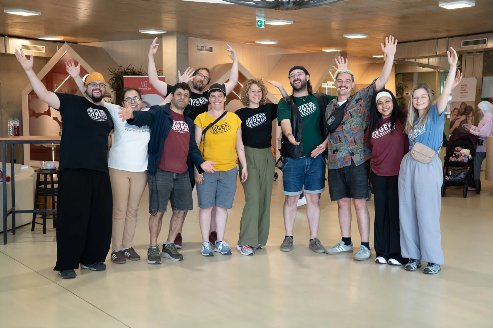 Gruppe erwachsener Personen posiert mit erhobenen Armen in einer hellen Halle.