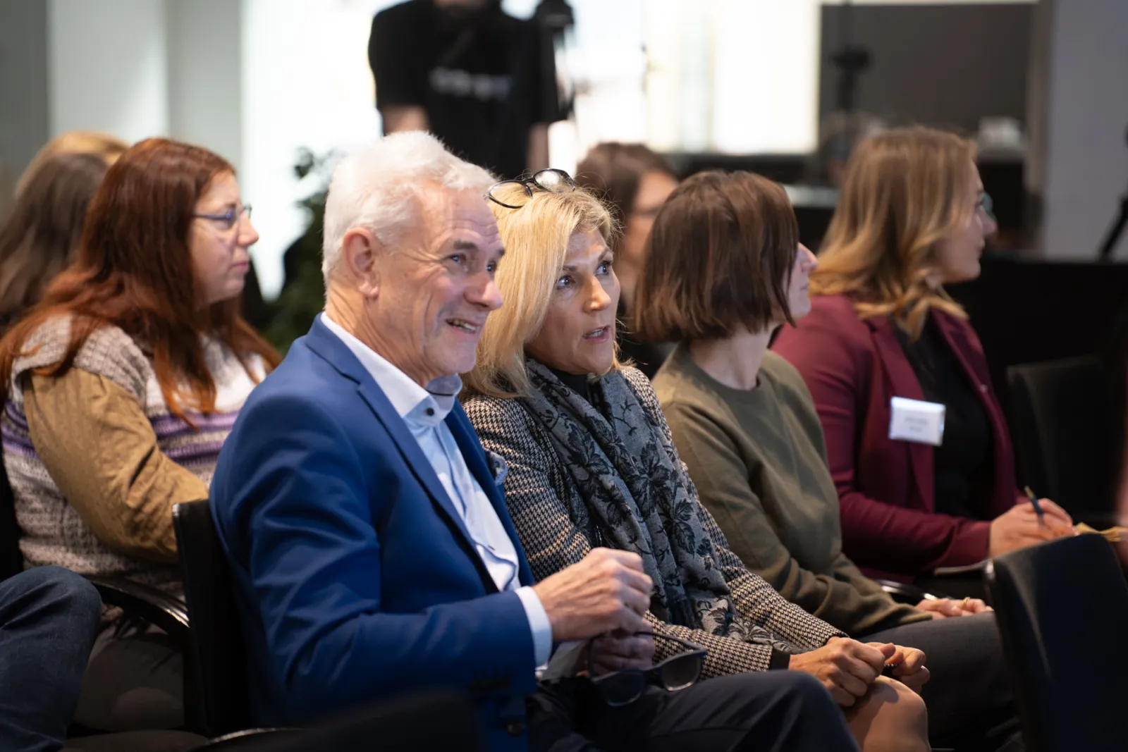 Gruppe erwachsener Teilnehmer lauscht aufmerksam einem Vortrag in einem Konferenzsaal.