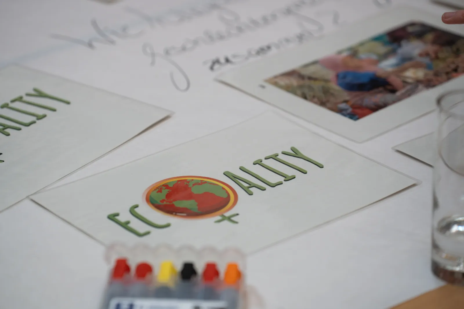 Karten mit Globus-Symbol und grünem Schriftzug liegen auf weißem Tisch; Marker-Set im Vordergrund.