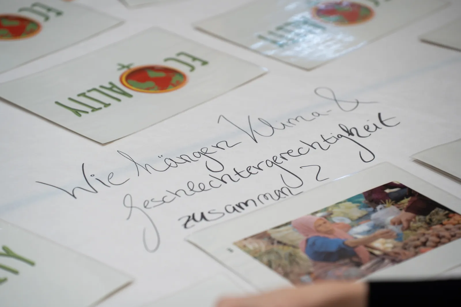 Handschriftliche Karte mit Frage zur Gerechtigkeit liegt auf einem Tisch, umgeben von weiteren Karten mit Weltkugel-Logo.