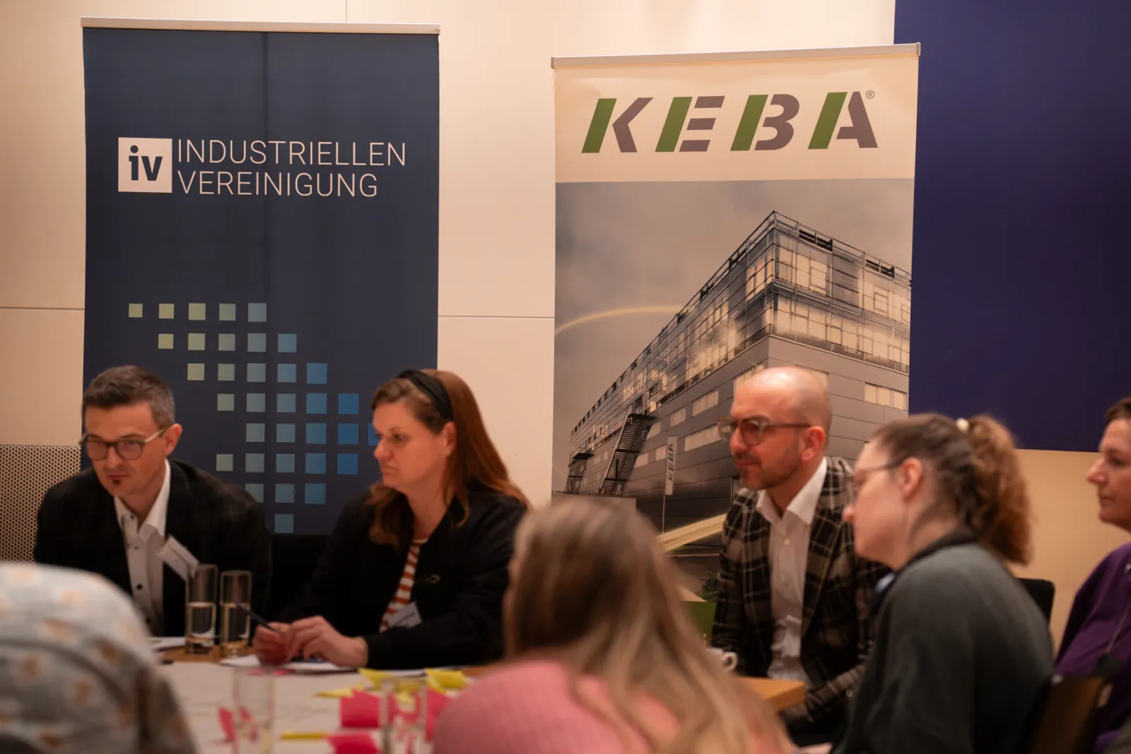 Gruppe von Fachleuten sitzt am Tisch und bespricht; Banner links zeigt iv INDUSTRIELLEN VEREINIGUNG, Banner rechts KEBA im Hintergrund.