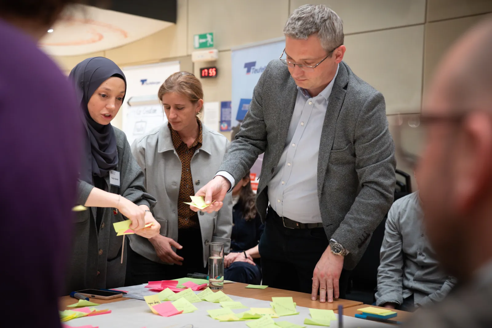 Gruppe von Workshop-Teilnehmern verteilt Haftnotizen auf einem Tisch im Konferenzraum