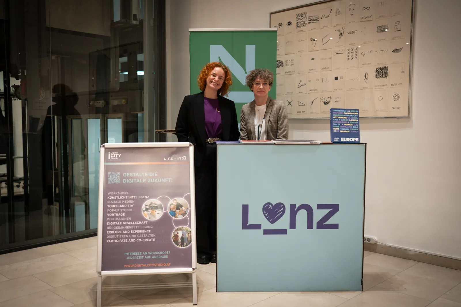 Zwei Frauen stehen hinter einem Lonz-Informationsstand in einer Lobby; links ein Plakat zur digitalen Zukunft.