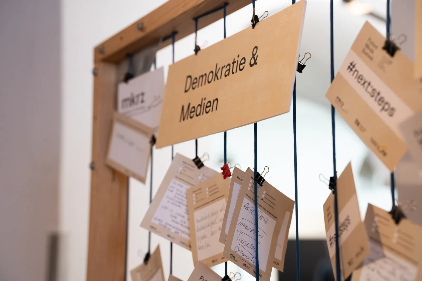 Holzrahmen-Display mit hängenden Karten an Schnüren; Schild „Demokratie & Medien“ – Ausstellungsinstallation