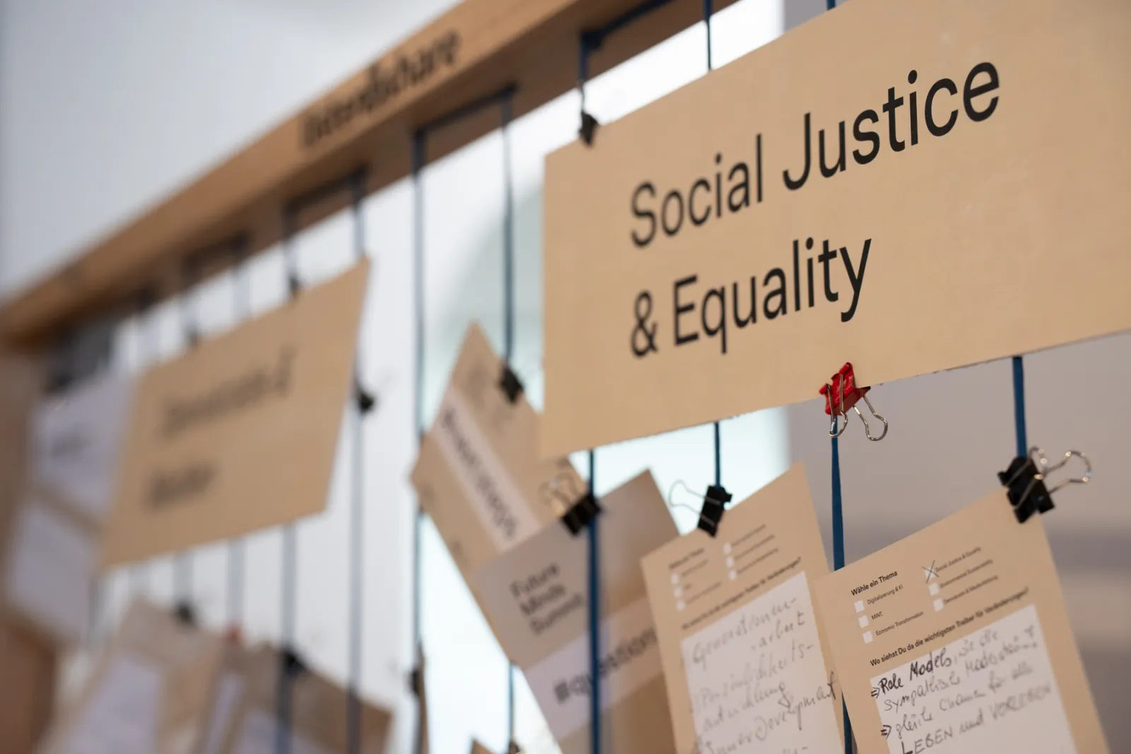 Großes Schild mit der Aufschrift "Social Justice & Equality"; hängende Zettel an Clips im Ausstellungsraum.