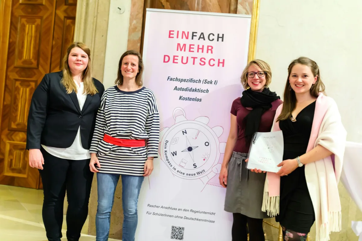 Vier Frauen posieren neben Banner 'EINFACH MEHR DEUTSCH' bei einer Veranstaltung; eine hält Urkunde.