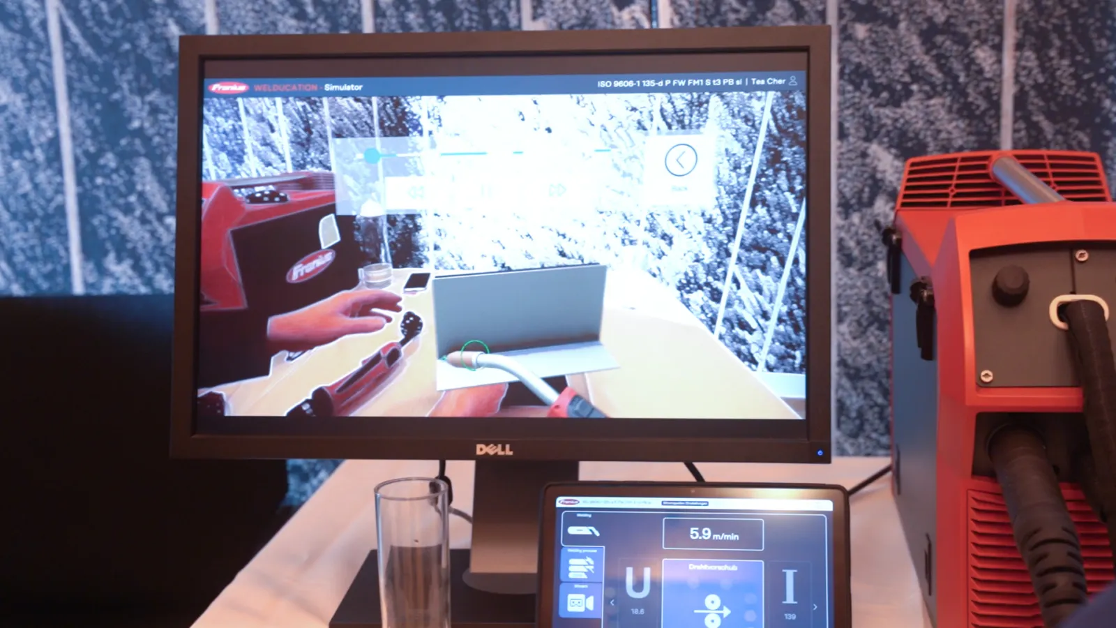 Dell-Monitor zeigt Schweiß-Simulator; eine Hand bedient Schweißbrenner am Tisch, daneben rotes Schweißgerät.
