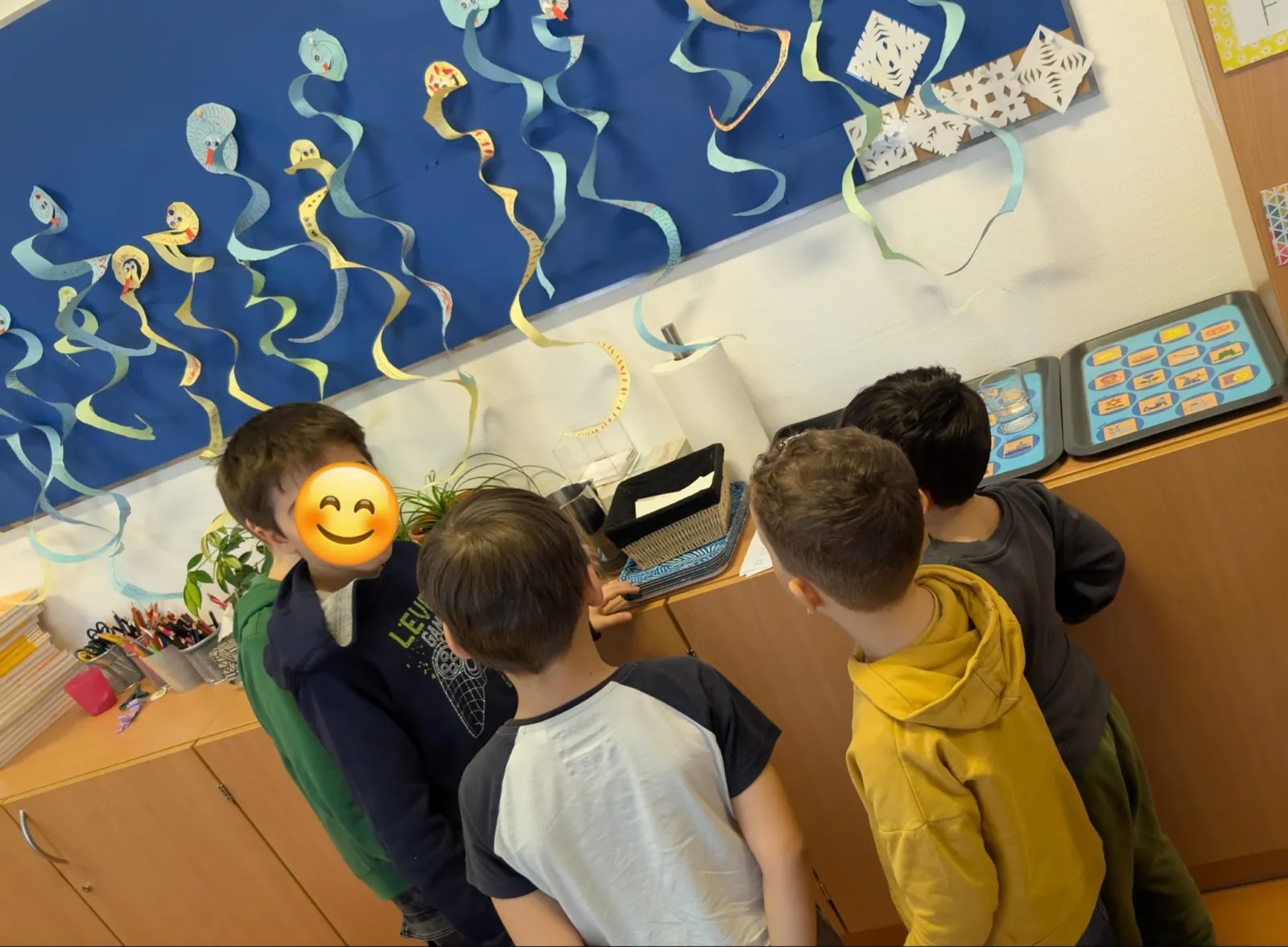 Vier Kinder im Klassenzimmer stehen um einen Tisch und betrachten Lernmaterialien in Behältern.