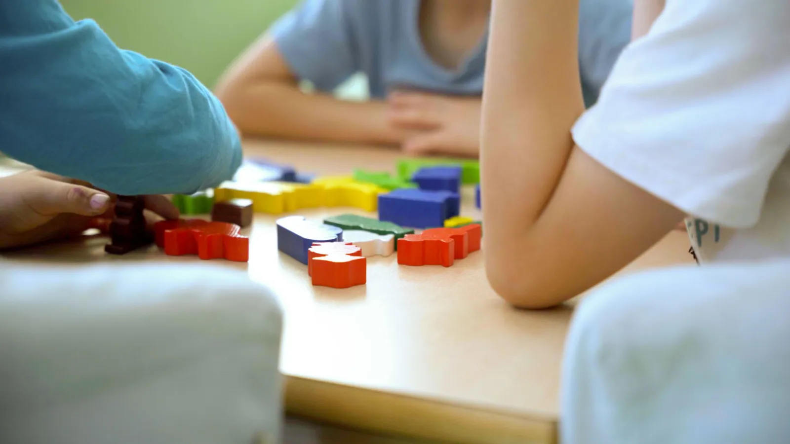 Mehrere Kinder spielen mit bunten Holzbausteinen auf einem Tisch; Nahaufnahme von Händen beim Sortieren.