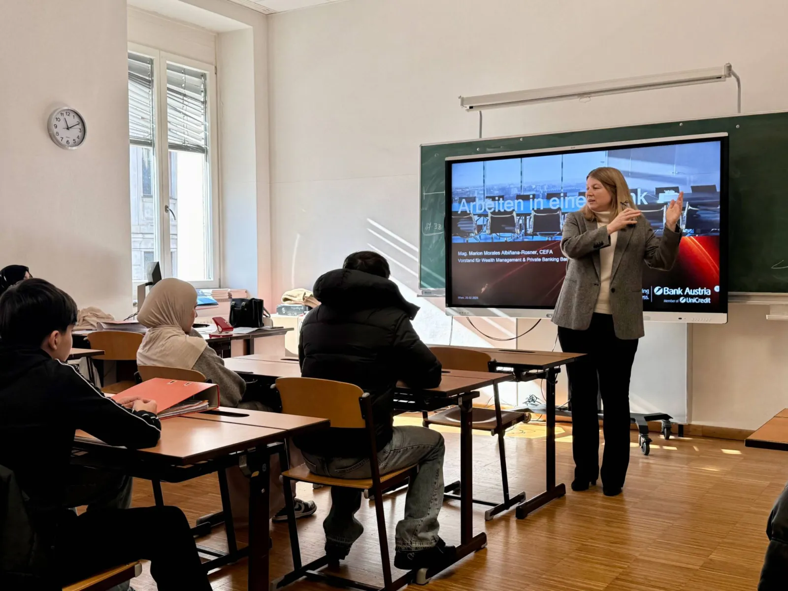 Lehrkraft präsentiert Unterricht an interaktivem Bildschirm vor der Klasse.