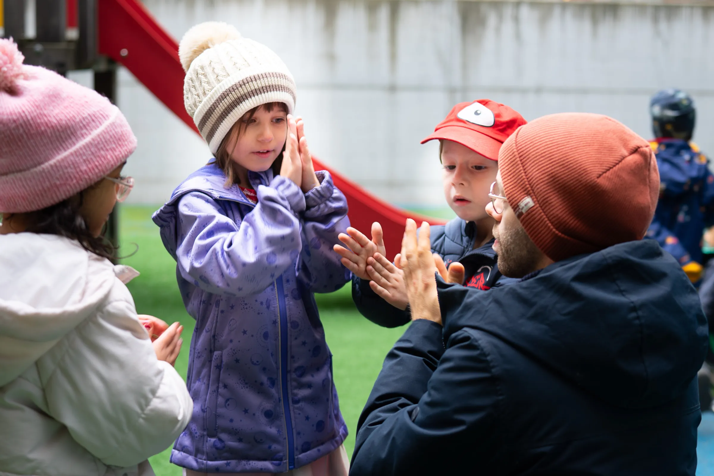 Kindergruppe klatscht Hände mit einer erwachsenen Begleitperson auf einem Spielplatz.