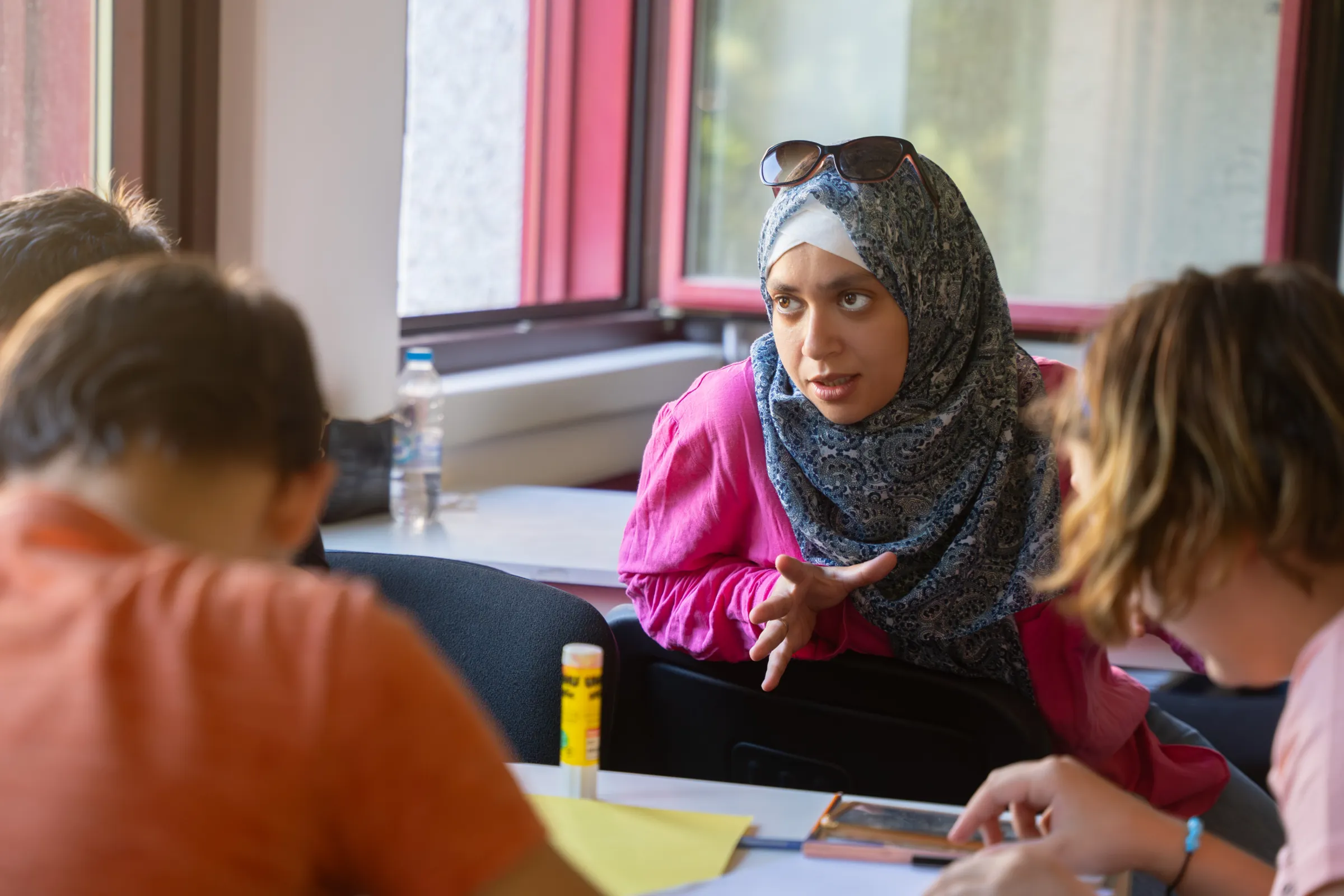 Person im Hijab erklärt während einer Gruppendiskussion an einem Tisch in einem Seminarraum.