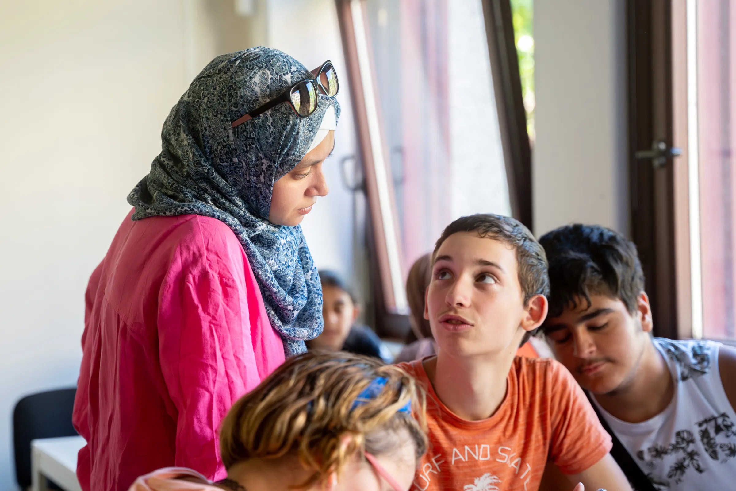 Person mit Hijab unterhält sich mit jugendlichen Schülern in einem Klassenraum.