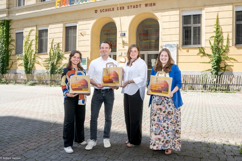Vier Erwachsene posieren vor dem Schulgebäude der Stadt Wien und halten BILLA-Geschenktaschen.