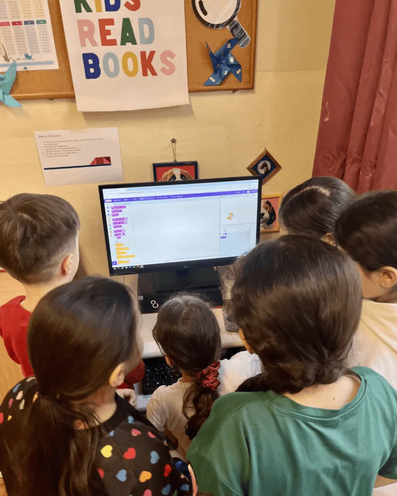 Gruppe von Kindern versammelt sich um einen Computerbildschirm und programmiert mit Scratch im Klassenzimmer.