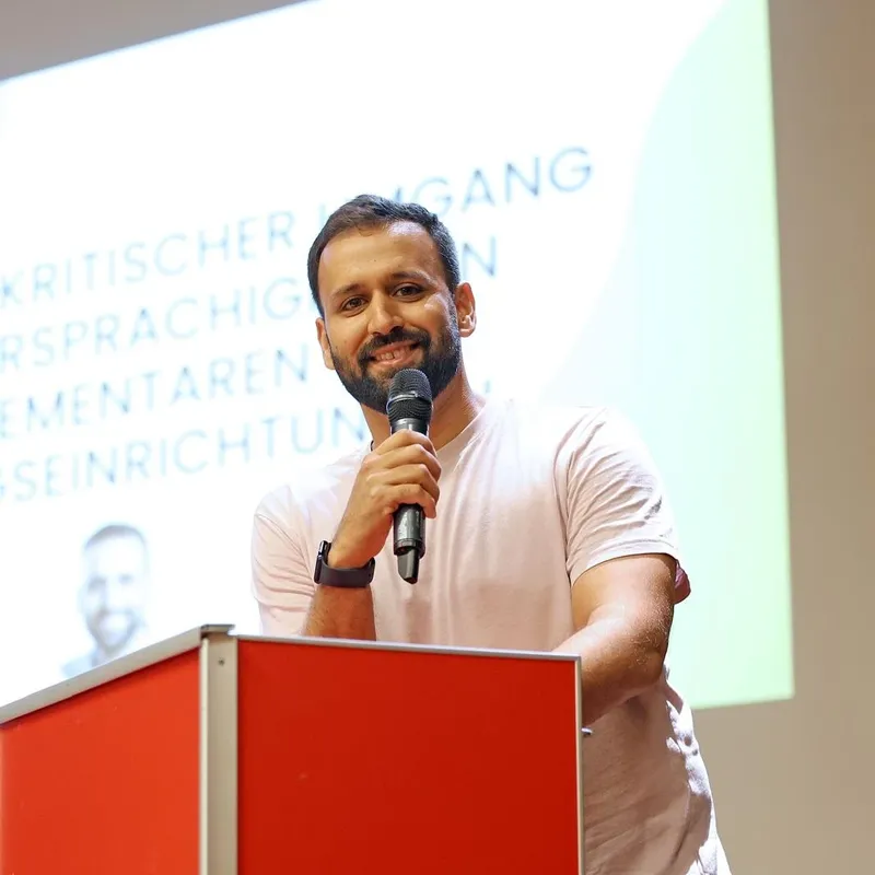 Sprecher steht hinter dem roten Rednerpult auf der Bühne und spricht ins Mikrofon.